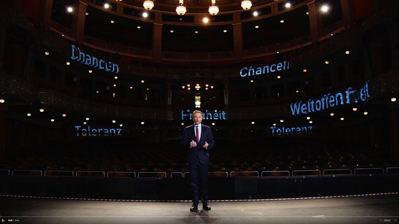 Eine finale Aufnahme der FDP-Dreikönigstreffen-Sendung, die Christian Lindner bei seiner Keynote-Rede zeigt, ergänzt durch Augmented-Reality-Grafiken mit den Worten 'Freiheit' und 'Toleranz'.