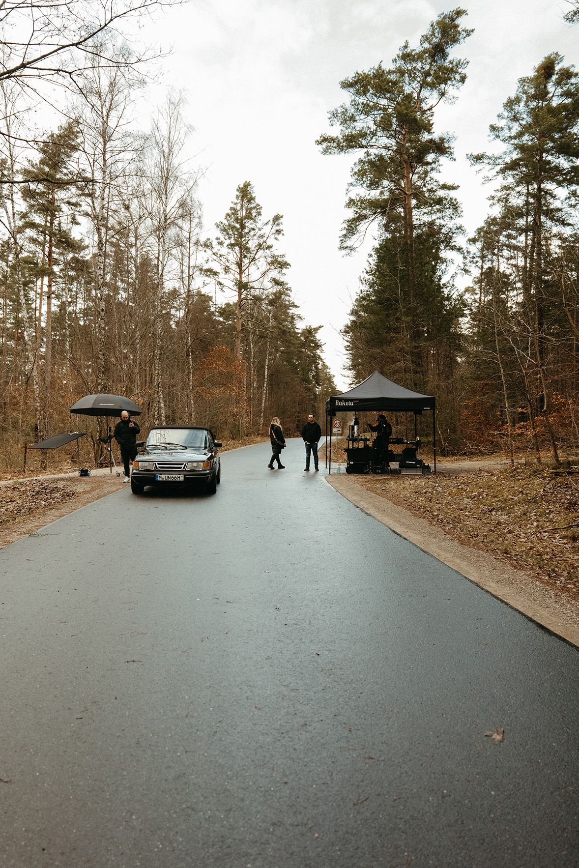 The Visionary Berlin production crew on a wooded road, managing the on-location filming of a driving scene with the classic Saab for the 'alles außer autos' brand film.