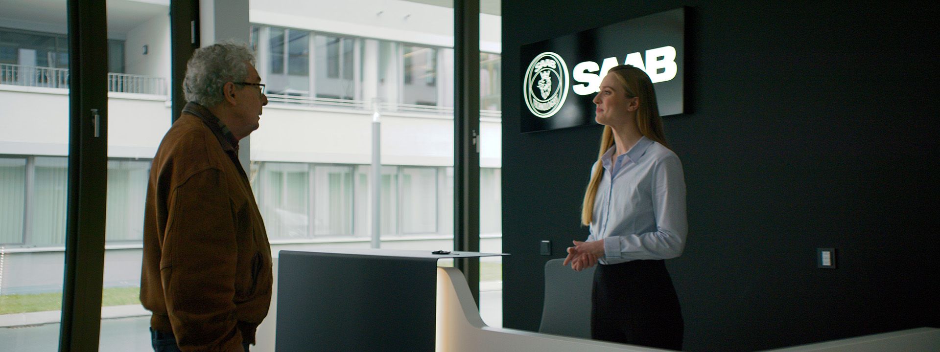A key scene from the 'Saab - alles außer autos' film where the protagonist, representing brand heritage, meets a modern employee at the Saab Technologies reception, symbolizing the company's evolution.